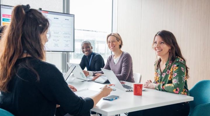 A diverse group of professionals collaborates at a conference table, using laptops and engaged in discussion