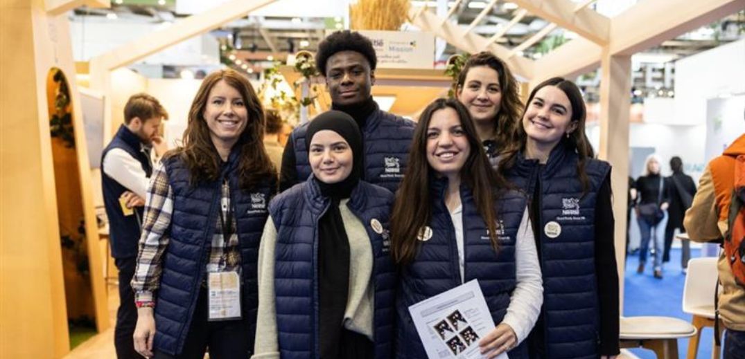 A group of seven individuals wearing blue vests pose together in a bright, modern exhibition space