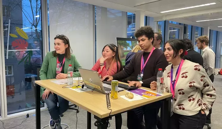 Un groupe de quatre personnes travaille ensemble autour d'un ordinateur portable dans un espace de travail moderne.