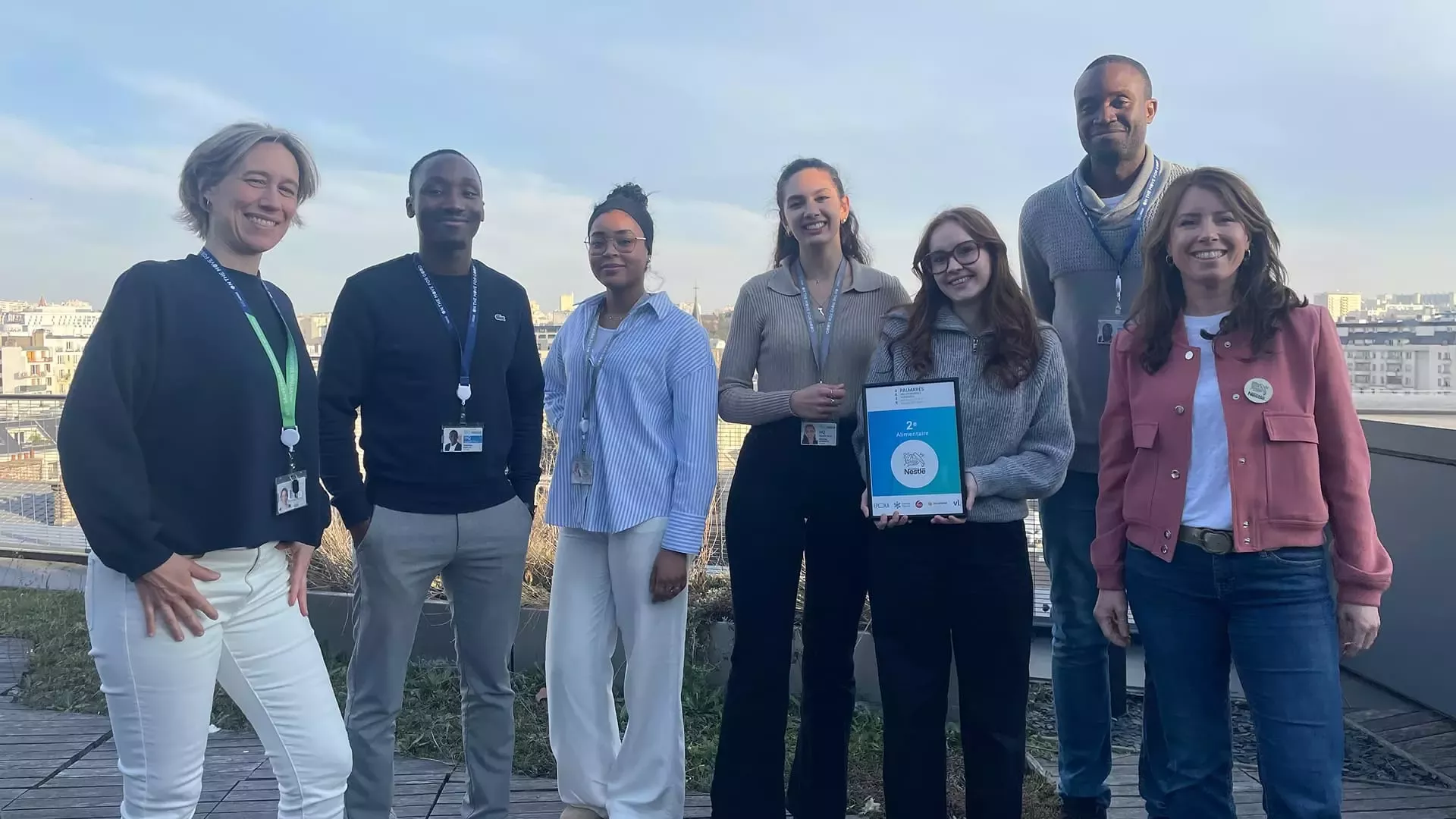 Un groupe diversifié de sept professionnels se tient sur un toit, tenant un prix tout en souriant